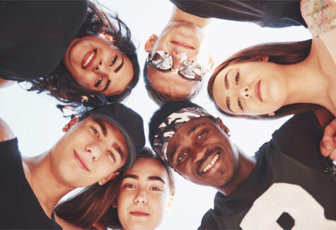 Group of diverse students huddled in a circle looking down at the camera and smiling