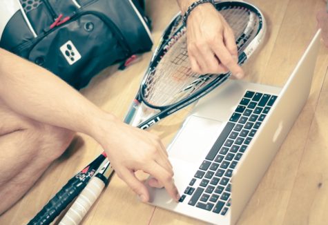Two squash players with their equipment gathered around a laptop computer