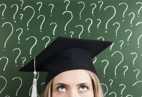 A graduating senior in her cap standing in front of a chalk board covered in question marks
