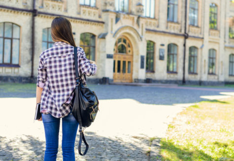 A female student preparing to enter a large stone-fronted university building