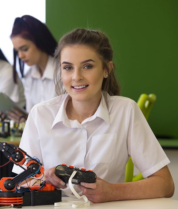 A smiling female student in uniform holding a remote control while working on a robotics project