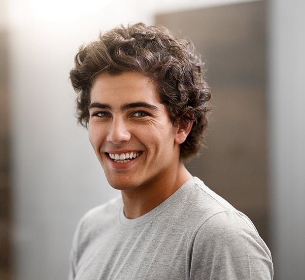 A male student in a gray shirt smiling indoors with a blurred background