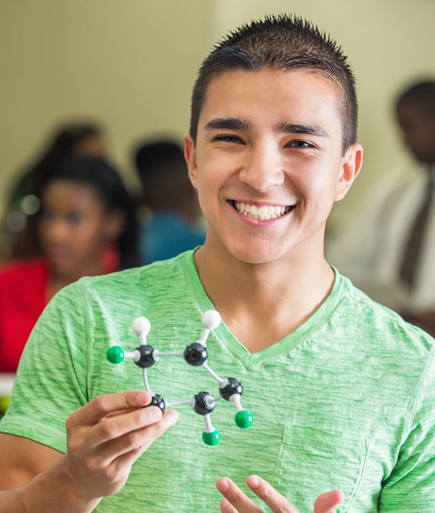 A male student holding a molecular model and smiling in a science classroom