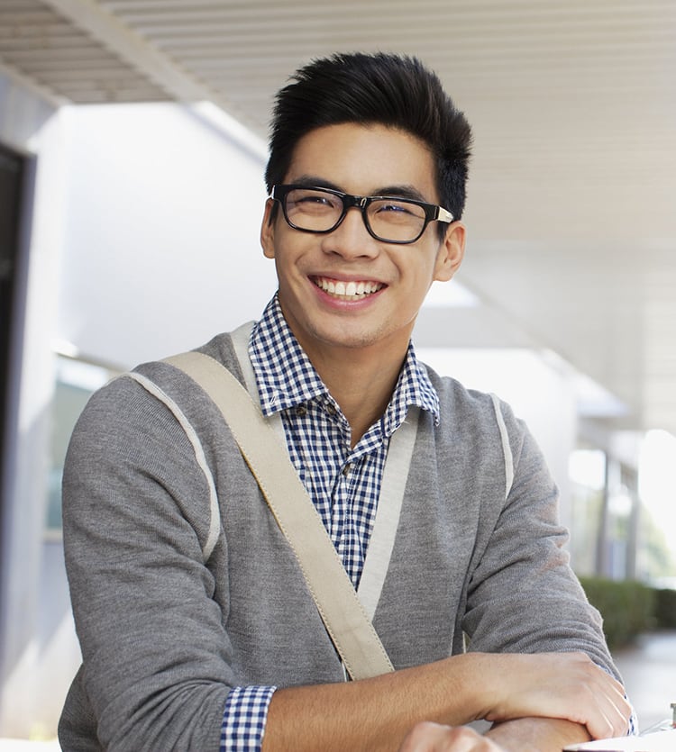 A young male student wearing glasses smiling outside a school building