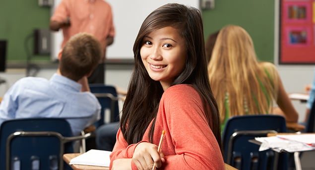 A closeup on a teenage female student in a classroom turning in her desk seat to look at you