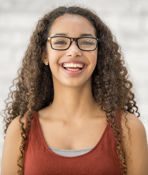 A female student with curly hair and glasses smiling in front of a light background