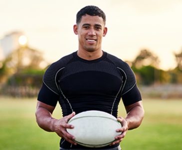 A college athlete holding a rugby ball while standing on a field