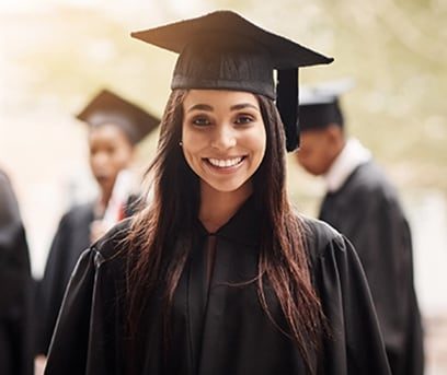 A high school girl graduate in a cap and gown with classmates in background