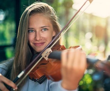 Close-up of high school girl with long blonde hair playing violin with a focused expression