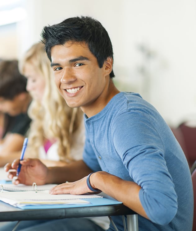 A male student smiling while writing in a notebook during class