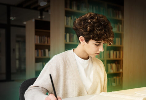 A student with short curly hair studying alone at a desk in a library