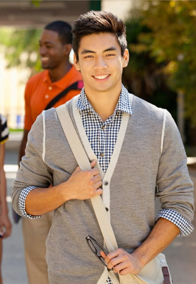 A young man smiling confidently outdoors with a bag over his shoulder
