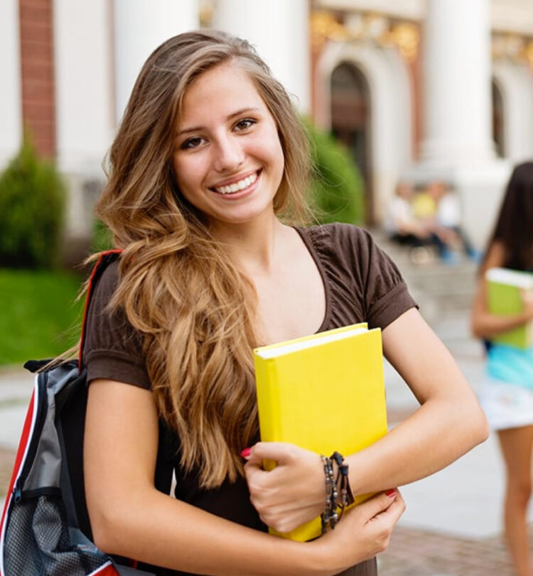 Young woman smiling and holding a yellow notebook on campus