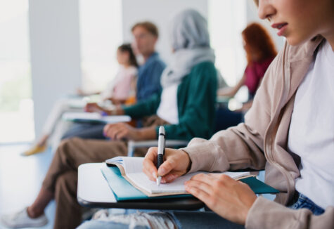 Close-up of students in a classroom writing in notebooks on individual desks