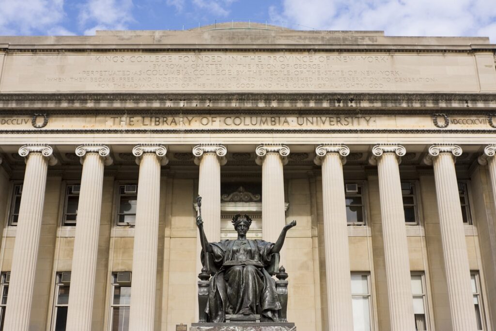 The front of Columbia University's library features tall columns and a statue in the foreground