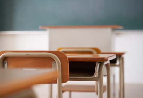 Empty classroom desks and chairs with a chalkboard and teacher's podium in the background