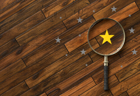 A magnifying glass highlighting a gold star among gray stars on a wooden surface, symbolizing selection or recognition