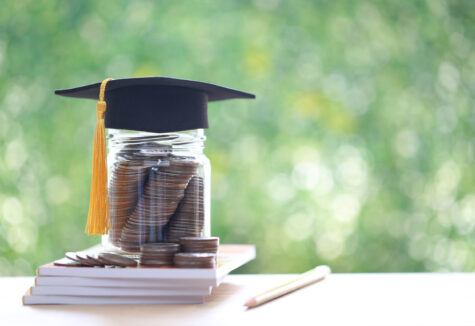 A graduation cap placed on a jar full of coins stacked on top of books, symbolizing saving for education