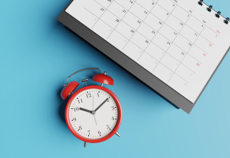 A red alarm clock next to a calendar on a blue background, showing a focus on time and planning