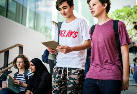 Two male students walk down stairs chatting, while others sit reading and studying in the background