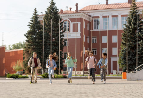 Five children run excitedly toward the camera in front of a red brick school building