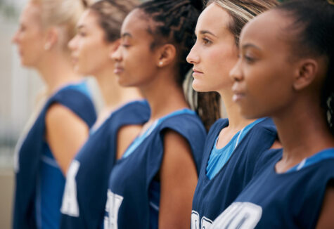 A row of focused female basketball players stands in matching blue uniforms, facing forward