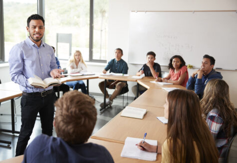 A male student standing at the front of a classroom, leading a discussion with engaged students