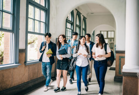 Group of students smiling and walking through a bright school hallway with backpacks