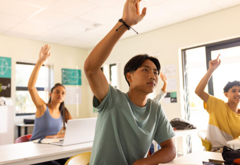 High school students raising their hands to participate in class while seated at desks.
