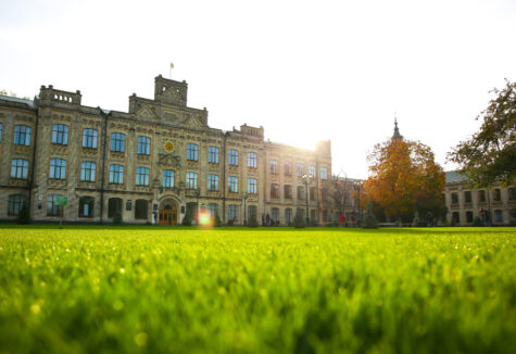Historic university building with large windows and a green lawn lit by the sun