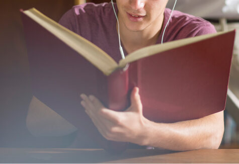 Close-up of a student reading a large red book while wearing earbuds