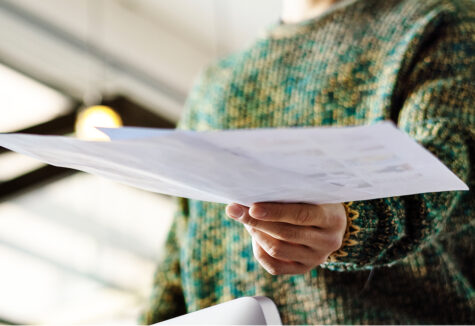 Close-up of a person in a green sweater handing over a document