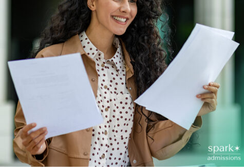 Smiling female student holding paperwork, wearing a polka dot shirt and tan jacket