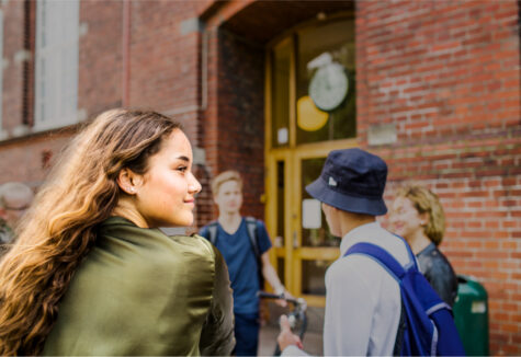 A group of students gather outside a brick school building, smiling and talking