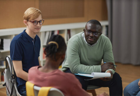 A black man as male psychologist talking to group teenagers in therapy session