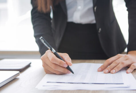 A person in business attire fills out a form on a desk with a pen